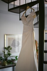 Vertical low angle shot of a white bride dress hung from a spiral staircase