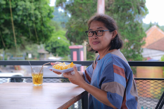 Woman sitting alone in her veranda enjoying some french fries and iced lemon tea