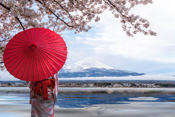Woman traveller with a red umbrella and walking over the bridge with Fuji mountain and Sakura flower