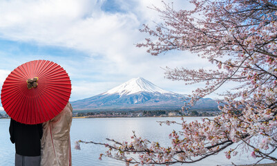 Couple traveller with a red umbrella and walking over the bridge with Fuji mountain and Sakura...