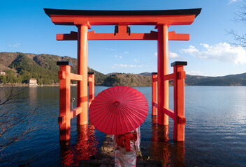 Asian couple in kimono wedding dress standing togather with red umbrella and red torii gate...