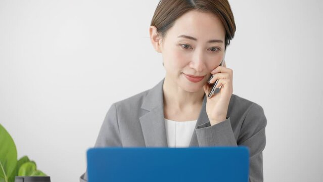 ノートパソコンを使いながらスマートフォンで通話をする若い女性　ビジネスイメージ