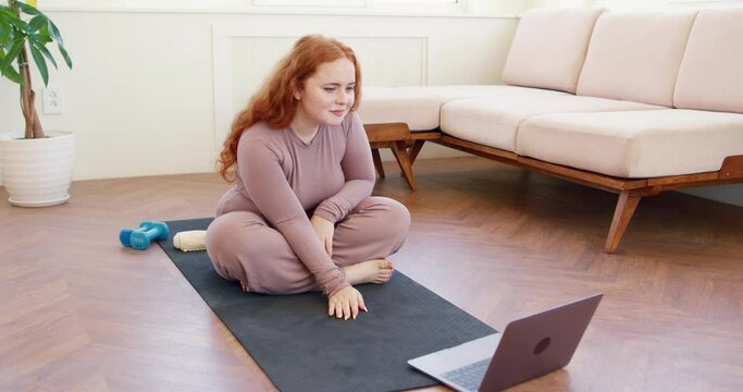 ginger obese woman watching sport video, taking part in fitness online maraphone, warming up arms, shoulders, doing exercises for arms, shoulders education covid-19, following online training lesson