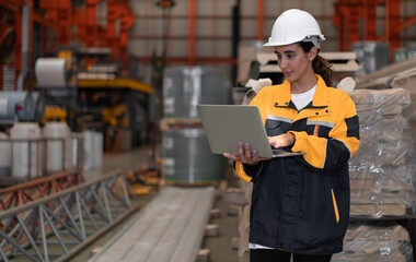 Female industrial engineer in white helmet and safety jacket work in heavy metal engineering factory. Latin technician woman worker using laptop computer in metalwork manufacturing facility, portrait. - obrazy, fototapety, plakaty