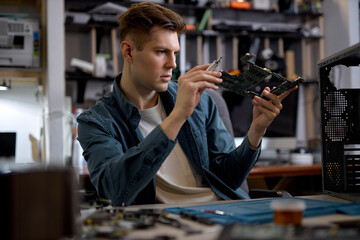 Confident caucasian man disassembles broken laptop. Computer service and repair concept. Laptop disassembling in repair shop, workshop. Electronic development by professional technician