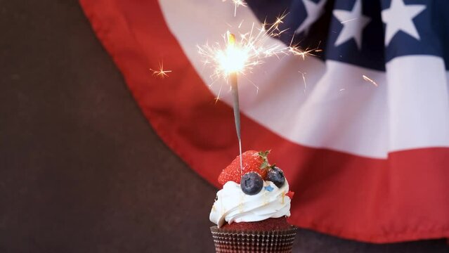 Fourth of july celebration. Sweet cupcake with blueberries and strawberry and sparkler over USA flag background