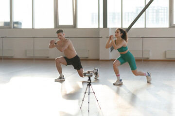 Young attractive couple, boy and girl exercising in gym, recording video, blogging about sports