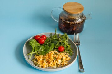 Fried scrambled eggs with spinach and tomatoes with tea on blue background