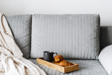 fresh pastry and mug with coffee on couch in stylish lounge room