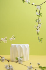 Light green background with geometric texture podium and cherry blossom branches. Still life. Spring concept. Vertical photo. Blurred foreground.