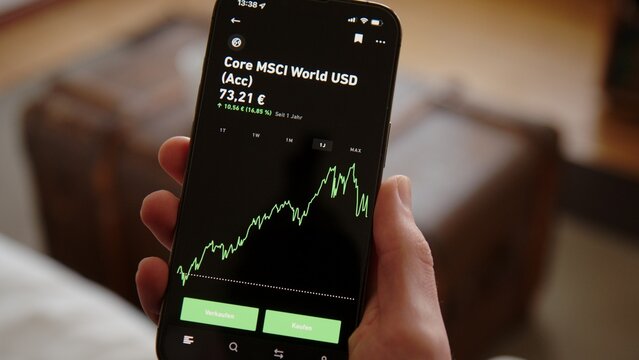 BERLIN - FEBRUARY 12, 2022: Hand opening Trade Republic App checking rising graph of ETF and Investments at home. Scrolling through MSCI World ETF page.  German Online Broker App.