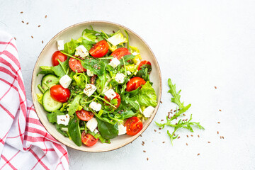 Green salad with spinach, arugula, tomatoes and feta with olive oil. Top view on white.