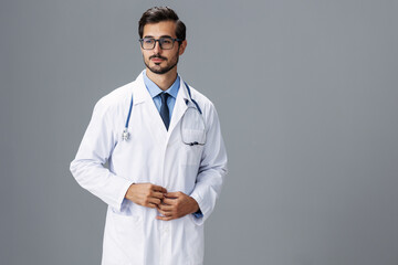 A serious doctor man in a white coat and eyeglasses and a stethoscope looks at the camera on a gray isolated background, copy space, space for text, health