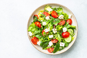 Spring salad in craft plate. Spinach, arugula, tomatoes and feta with olive oil. Top view on white.