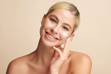 Beautiful young woman applying face cream on beige background, Face care, Facial treatment,...