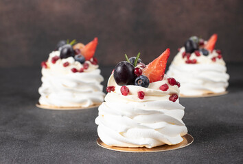 Mini Pavlova cake with strawberry, blueberry, pomegranate and grapes on dark gray background
