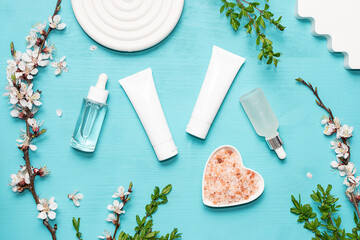 Set of cosmetic products for skin care and spa procedures on bright blue background  with clay decorations and blooming apricot branches top view.