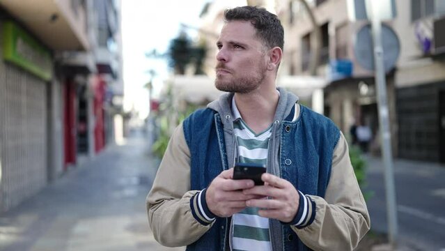 Young caucasian man smiling using smartphone at street