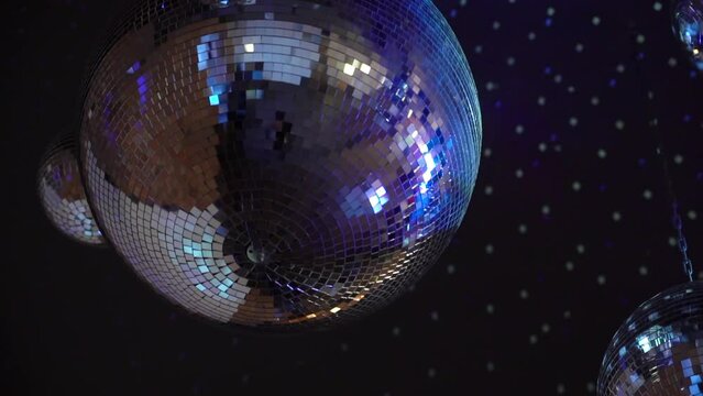 Silver mirror disco ball suspended from the ceiling rotates quickly, light spot rays and glare. White stage light at a concert hall, club, party or disco. Illumination and atmosphere.