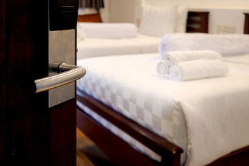 Opened door with blurred background of stack of fresh white bath towels on white bed in hotel room,...