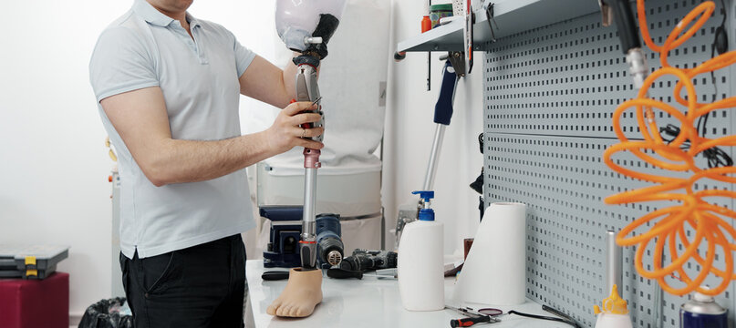 Crop unrecognizable craftsman adjusting and bending modern prosthetic leg at knee section at workbench in manufacturing factory - Powered by Adobe