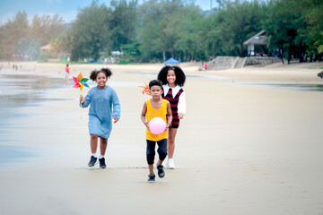 Obraz premium Cute groups of African kids have fun activity together on summer beach blue sea, two girls with black curly hair and boy running on tropical beach, happy childhood friends on holiday vacation.