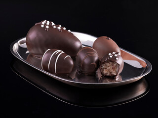 Silver serving platter with noble decorated marzipan chocolates on black background with reflections.
