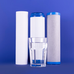 set three of cartridges for water filter with clear glass of water isolated on violet background....