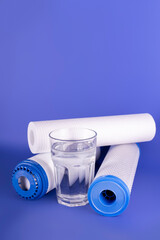 set three of cartridges for water filter with clear glass of water isolated on violet background. Concept of water treatment technology. filter cartridges to domestic water treatment systems.