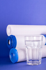 set three of cartridges for water filter with clear glass of water isolated on violet background....