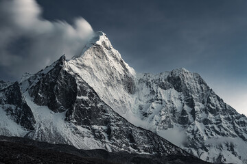 Snow capped Mount Ama Dablam and blurred fast moving clouds behind it in daylight, Nepal, Himalayas