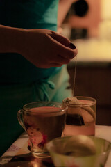 A woman brews a tea bag in a dark kitchen. Woman making two cups of tea