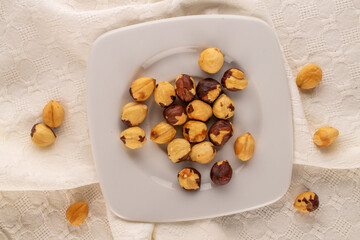 Roasted hazelnuts in a ceramic dish on a white linen napkin, close-up, top view.