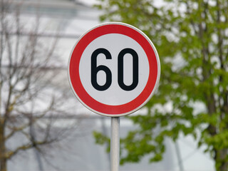 Selective focus shot of a Maximum Speed Limit 60 Street Sign with trees and building in the...