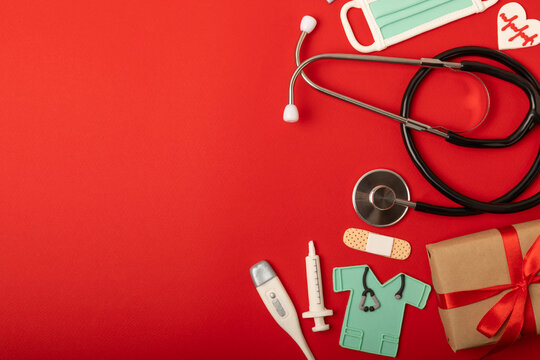 National Day of Doctors. Modern stethoscope, gift box and gingerbread in the form of medical supplies on a red background. .Gingerbread in the form of a thermometer, a medical mask, a pill, a patch.