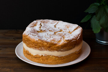 Tarta polaca de pasta choux rellena de crema con azúcar glas por encima. Tarta Karpatka en plato...