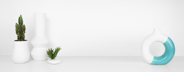 Fototapeta na wymiar Modern home decor and plants on a shelf. Geometric vases, succulent and cactus on a white shelf against a white wall background. Banner with copy space.