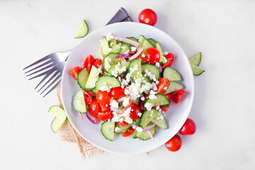 Greek salad with cucumber, tomatoes and feta cheese. Top down view with frame of ingredients over a marble background.