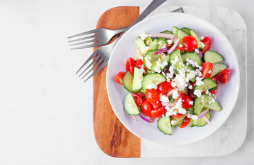 Greek salad with cucumber, tomatoes and feta cheese. Overhead view on a marble background.