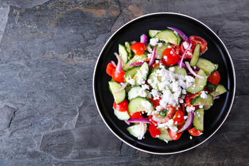 Greek salad with cucumber, tomatoes and feta cheese. Above view on a dark stone background.
