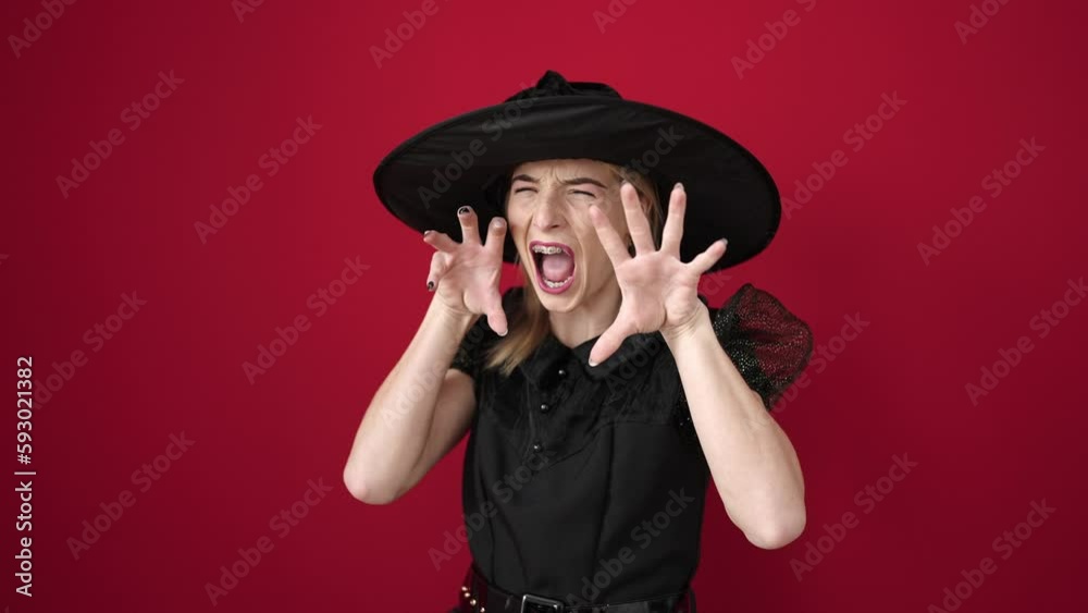 Poster young blonde woman wearing witch costume doing scare gesture over isolated red background