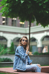 Obraz premium Hipster girl in clean white t-shirt and jeans posing against the background of buildings, minimalist urban clothing style