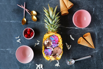 Summer ice cream in a pineapple. Top down view table scene on a dark stone background.