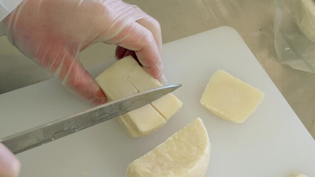 A woman in a white coat and gloves cuts Robiola, caprino cheese. Close-up, slow motion 4k. Cheese tasting at the farm. Craft production, homemade italian cheese.