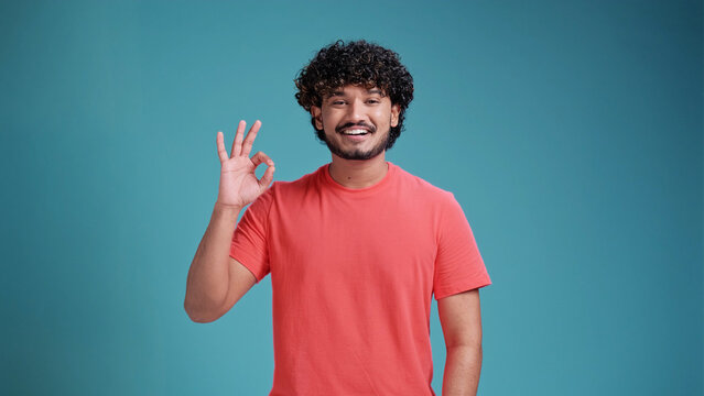 Everything is OK positive man showing OK sign . close up photo. gesture concept, in basic coral t-shirt isolated on a blue studio background