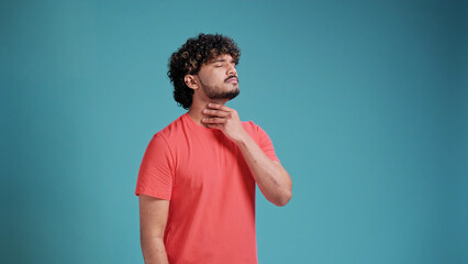 Indian man with beard wearing coral t-shirt touching painful neck, sore throat for flu, clod and infection on blue studio background