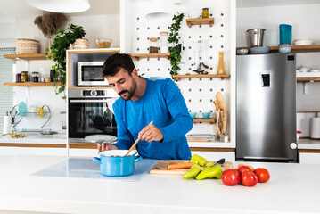 Smiling young bearded sporty man cooking salad, cutting fresh vegetables in modern kitchen, happy satisfied male preparing vegetarian snacks, food for dinner or party, enjoying leisure time, hobby