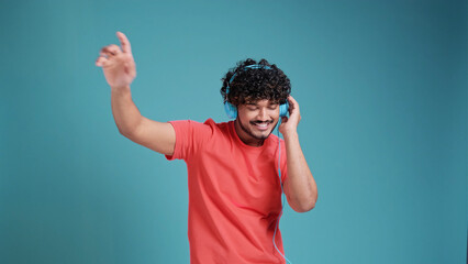 Young smiling happy cheerful student Indian man 20s dancing with headphones listen to music have...