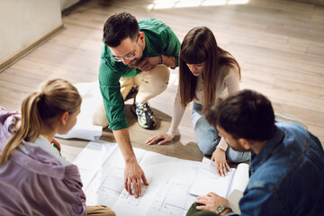 Young architects sitting on the floor and analyzing blueprints in the office