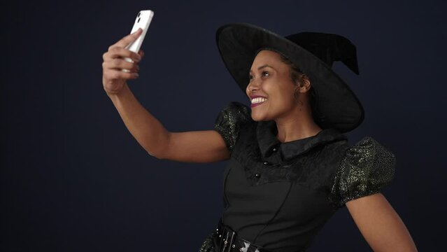 African american woman wearing witch costume make selfie by smartphone over isolated black background